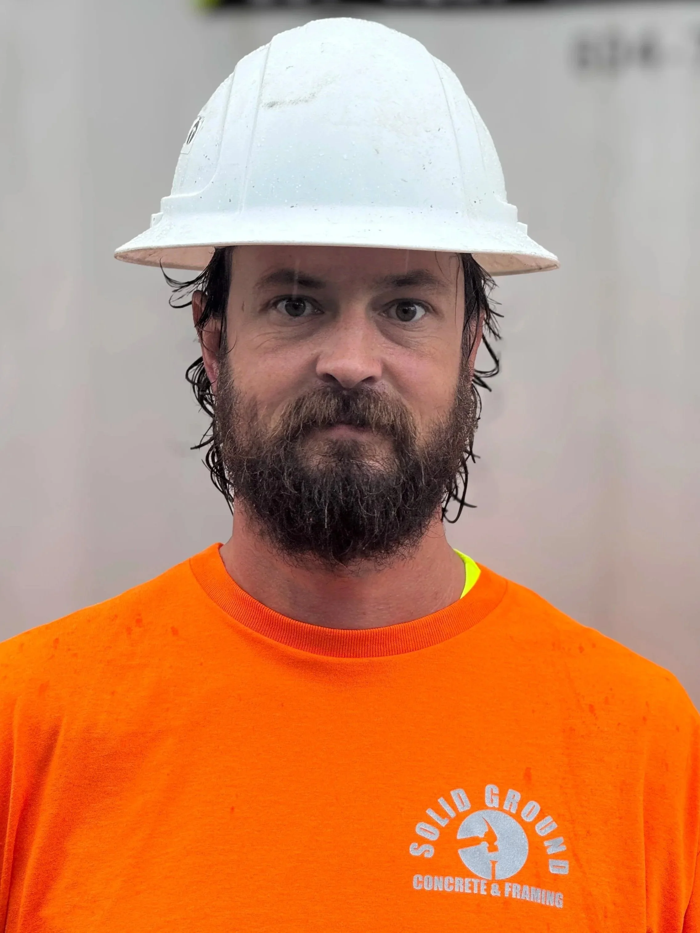 Man wearing an orange shirt with 'Solid Ground Concrete & Framing' logo, and a white hard hat.
