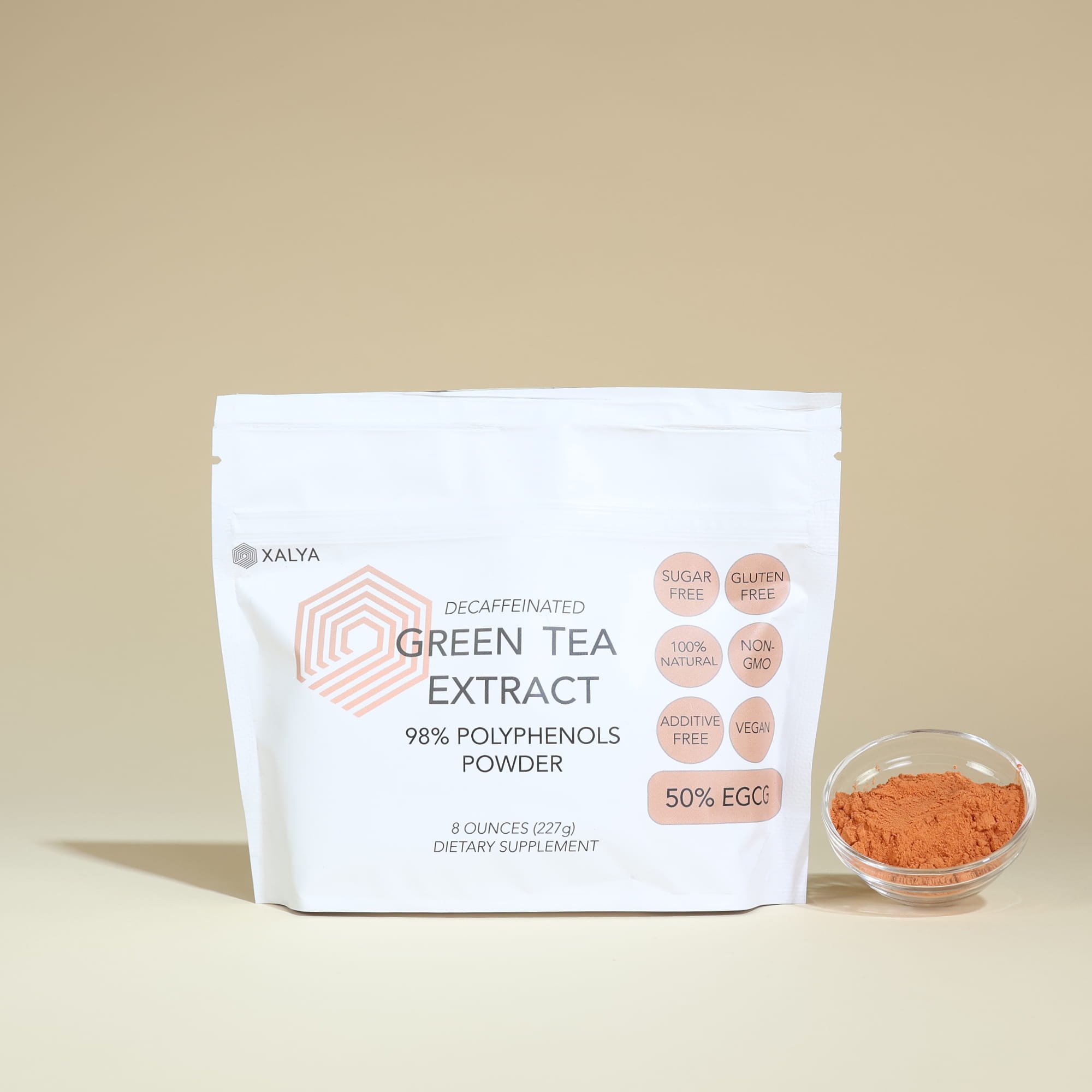 Stand up pouch of XALYA decaffeinated green tea extract powder with a small bowl of reddish-brown green tea extract powder next to it.