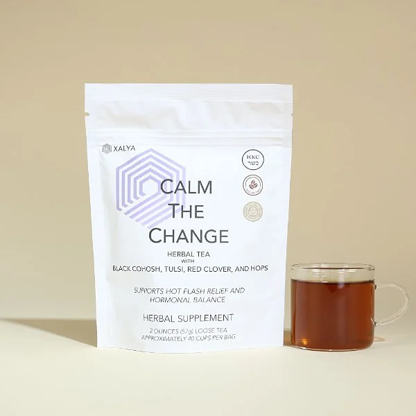 A white stand up pouch of XALYA Calm the Change herbal menopause support tea next to a glass cup of a brewed tea.