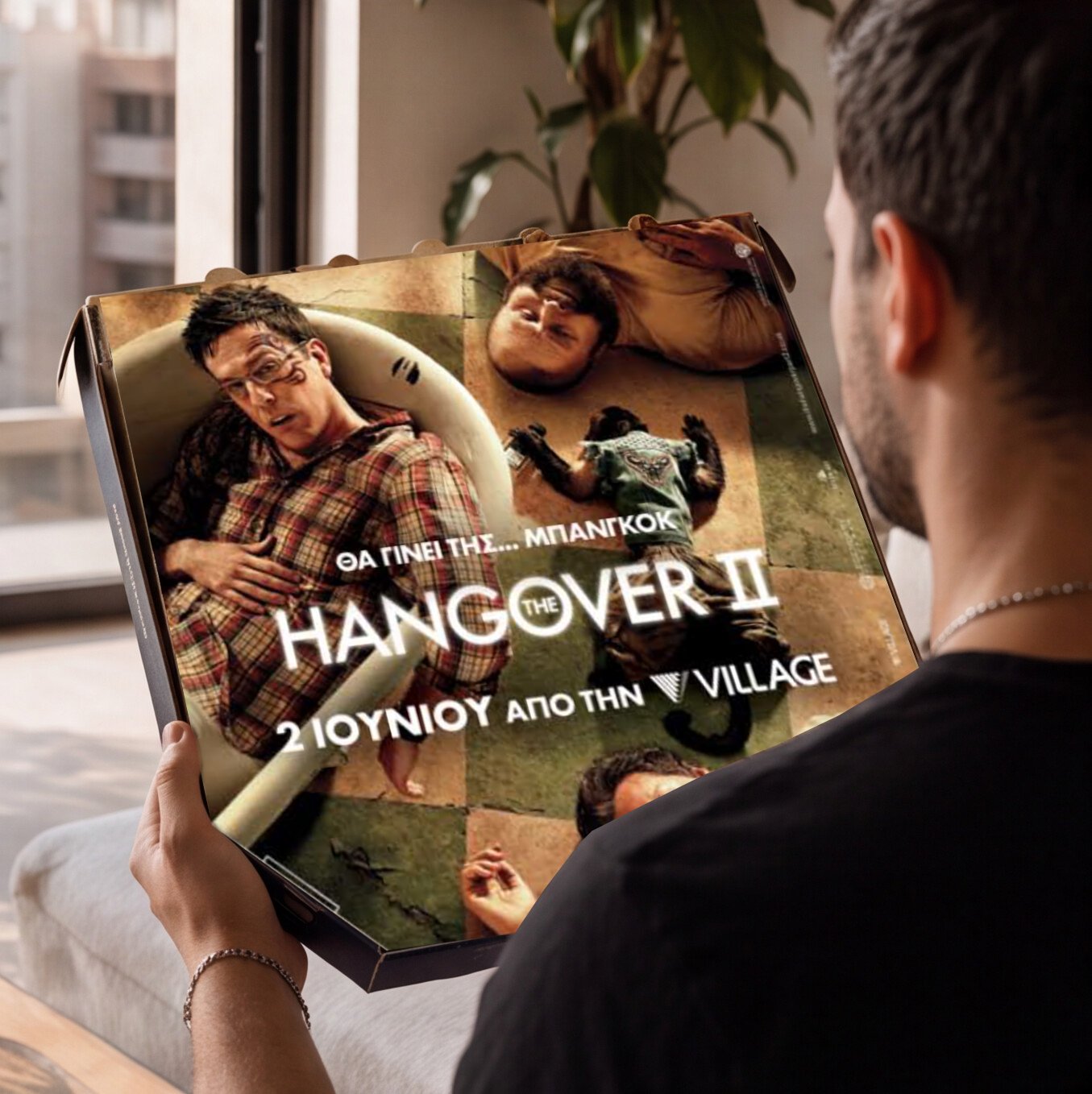 A person holding a movie poster for 'The Hangover Part II' featuring images of the main characters lying on the floor and relaxing in a hotel room. The poster includes Greek text indicating a Greek release date.