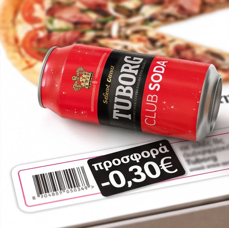 A crumpled red can of Tuborg Club Soda lies on a white surface next to a magazine or brochure with a barcode and a discount sticker showing -0.30€.