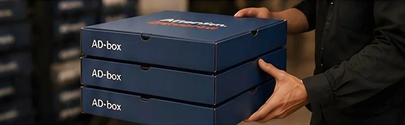 Person holding three stacked blue AD-box boxes in a store.