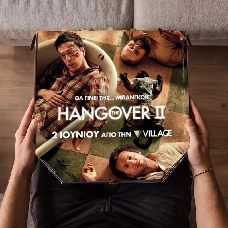 A person holding a box for the movie "The Hangover Part II" featuring three men lying on the floor, with Greek text indicating the release date of June 2nd from Village.