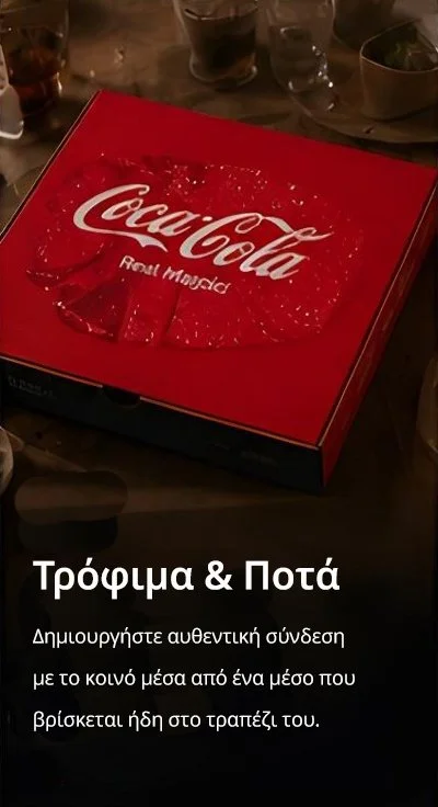 A red Coca-Cola pizza box on a table, surrounded by glasses and plates in a restaurant setting.