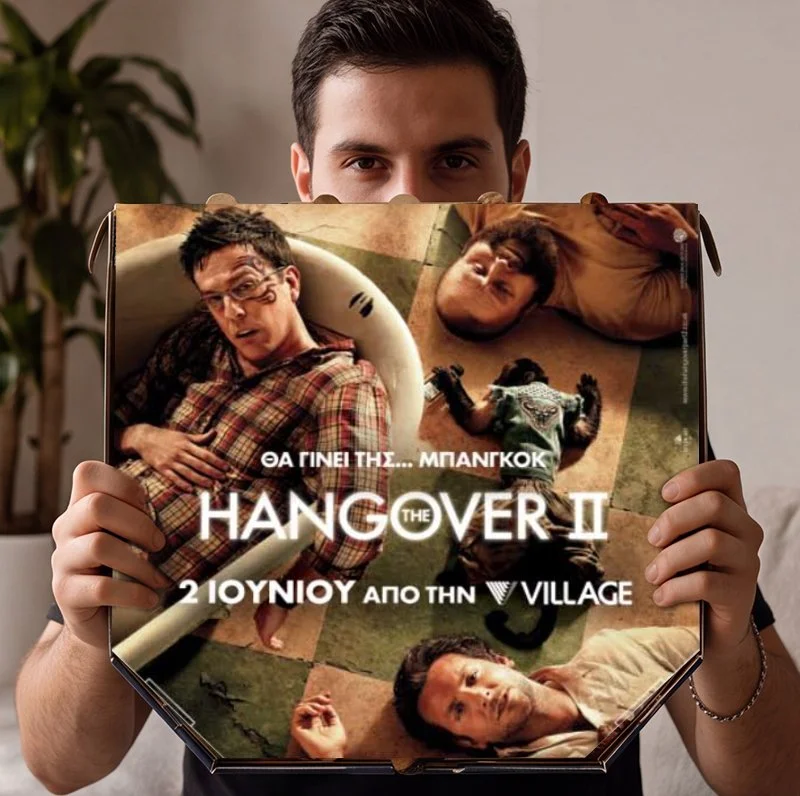 Person holding a movie poster for 'Hangover II' with Greek text.