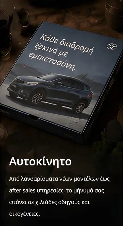 A pizza box advertisement for a new car, showing a black vehicle on the box, with Greek text that translates to "Every journey starts with confidence." The box has the Toyota logo and mentions reaching thousands of drivers through sales and services.