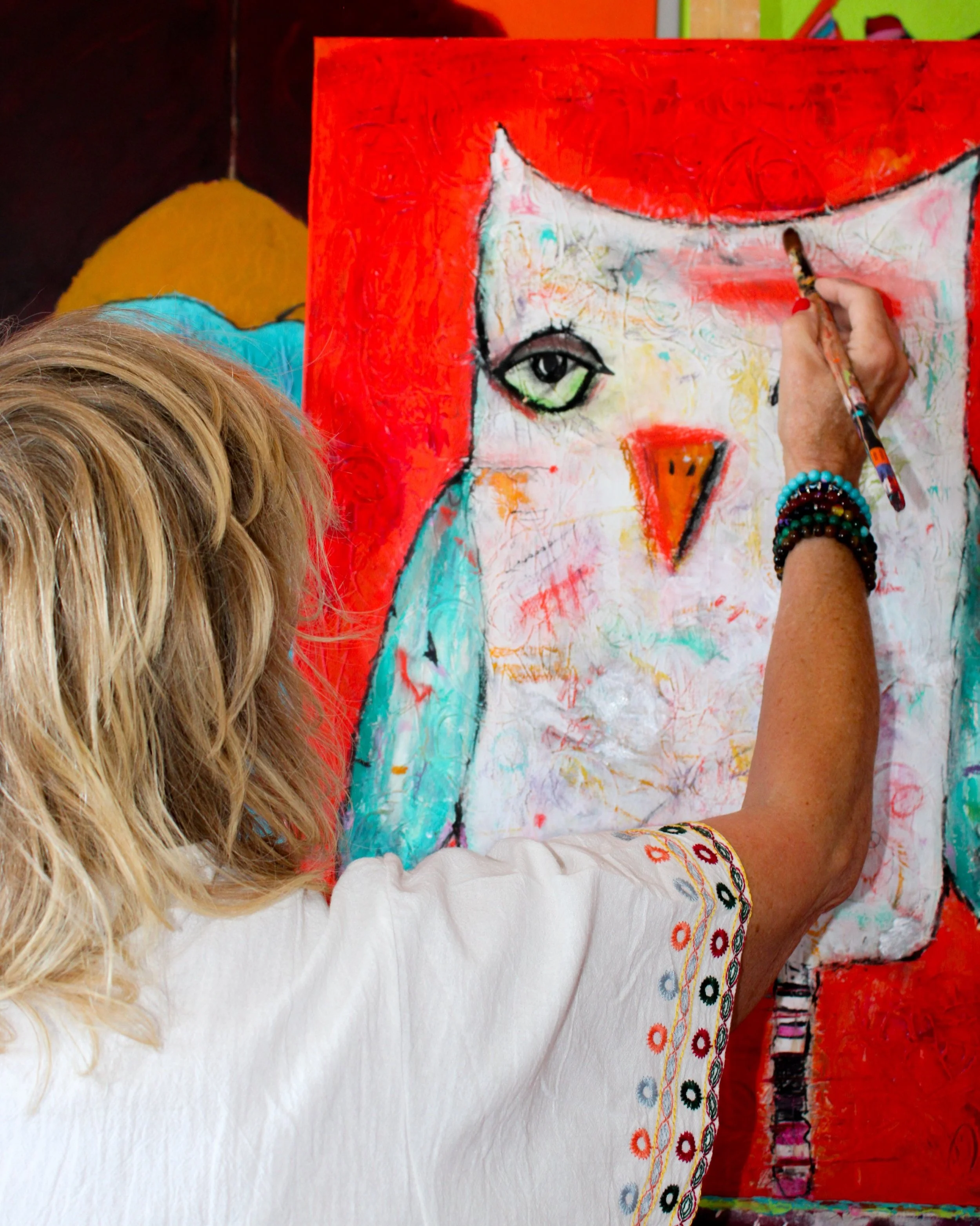 A person painting an abstract portrait of a cat with one eye on a red canvas, using bright colors and expressive brushstrokes.