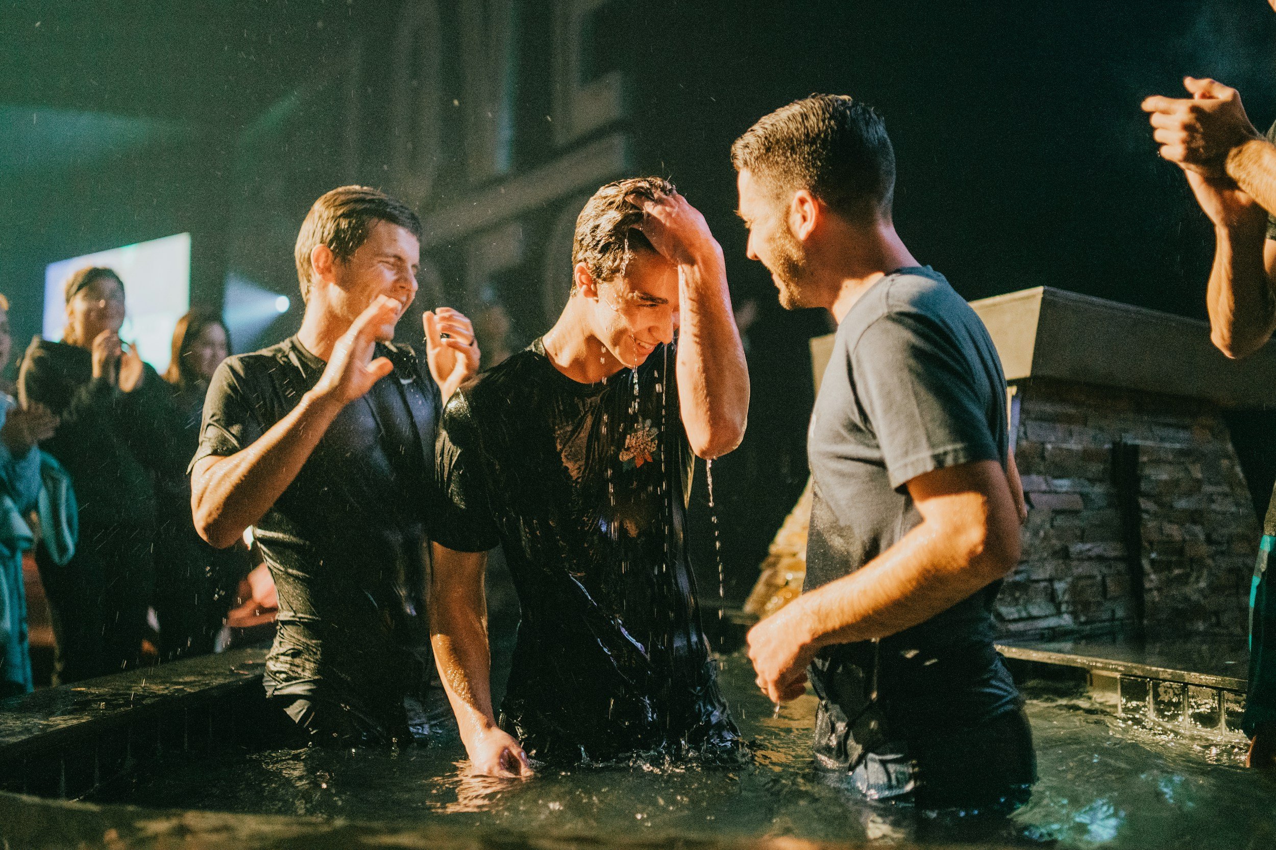 A group of people in a church baptism ceremony, with one man being baptized and others celebrating.