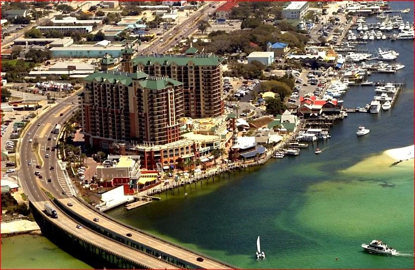 Aerial view of a coastal city with high-rise buildings, a marina filled with boats, and a bridge over a body of water.