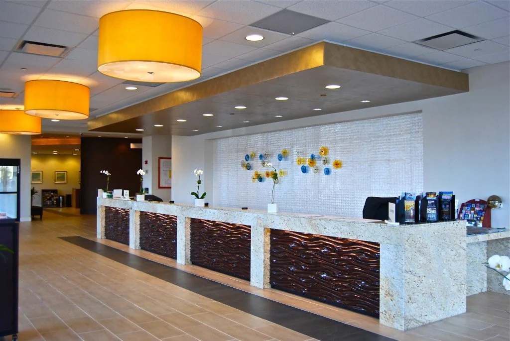 Hotel lobby reception area with a long granite counter, decorative wall art, and yellow pendant lights hanging from the ceiling.