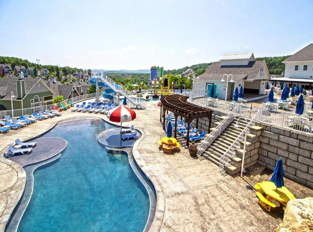 Empty outdoor swimming pool area with lounge chairs, umbrellas, and water slides on a sunny day