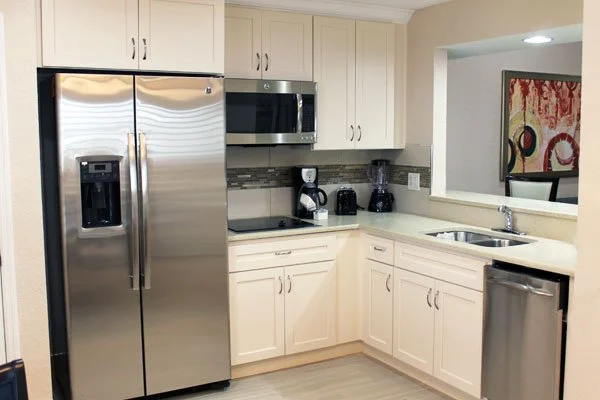 Kitchen with stainless steel refrigerator, microwave, sink, coffee maker, toaster, and cabinets with cream color finish.