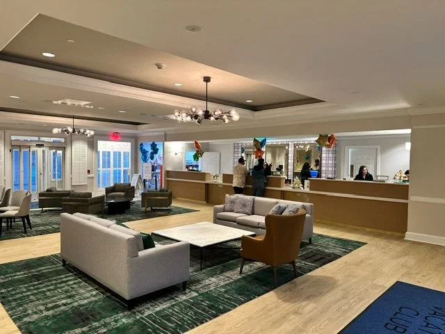 Hotel lobby with seating area, balloons, and people at the reception desk.