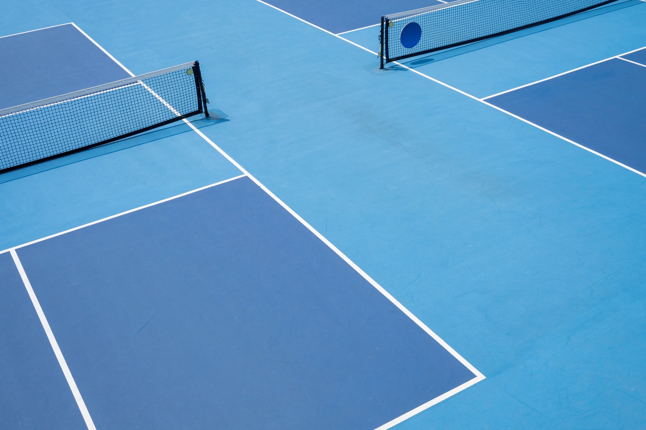 Empty blue indoor tennis courts with white lines and two nets.