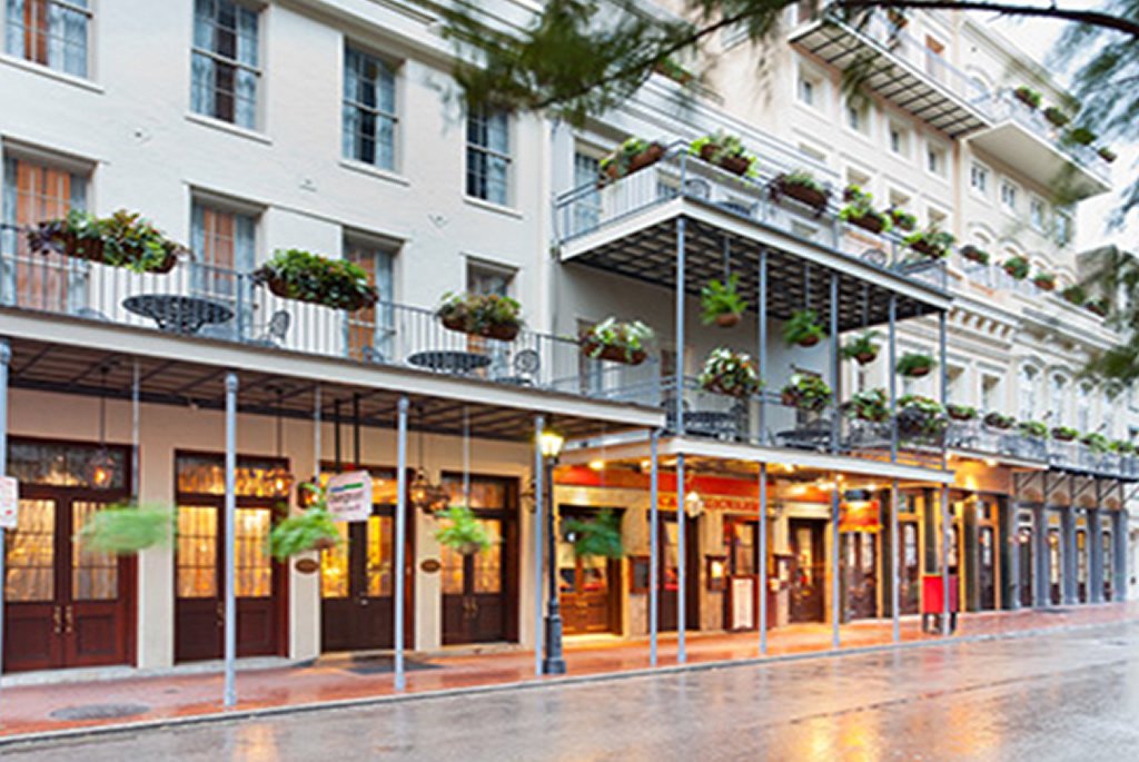 Empty street view of a building with balconies and potted plants, possibly in a city.