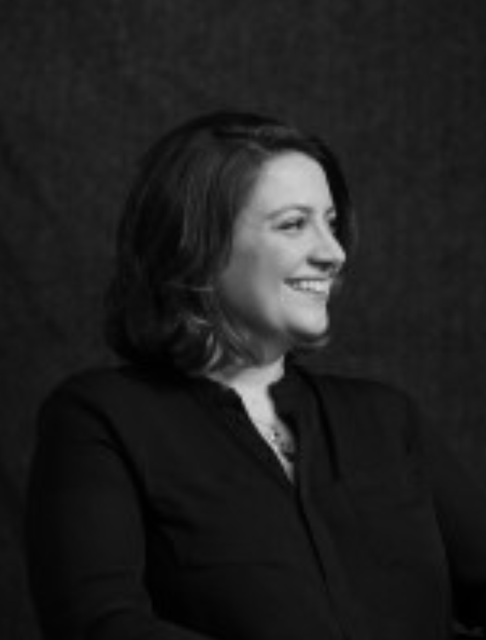 Black and white photo of a smiling woman with shoulder-length hair, wearing a dark top, looking to her right, against a plain dark background.