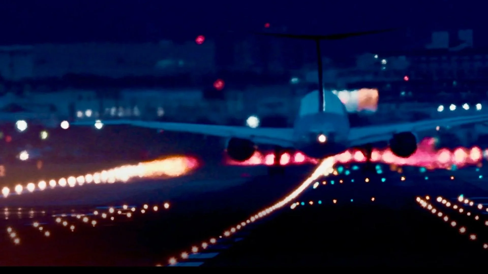 An airplane flying at night over a brightly lit highway with colorful lights and blurred background.