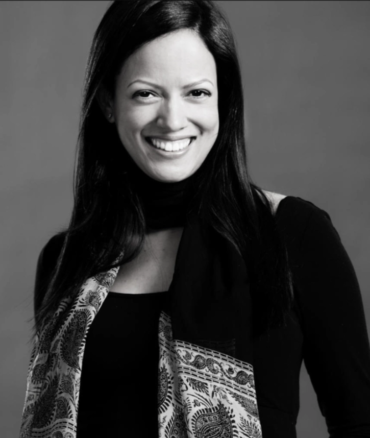 A smiling woman with long dark hair, wearing a black top and patterned scarf, black and white portrait.