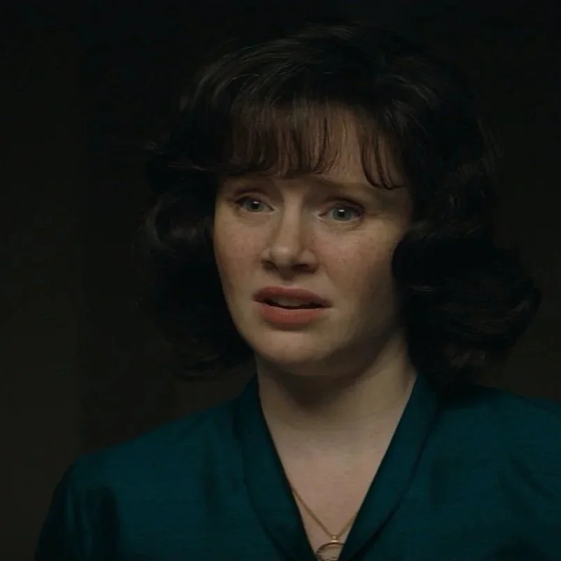 A woman with dark, curly hair wearing a teal top, displaying a distressed or shocked facial expression.