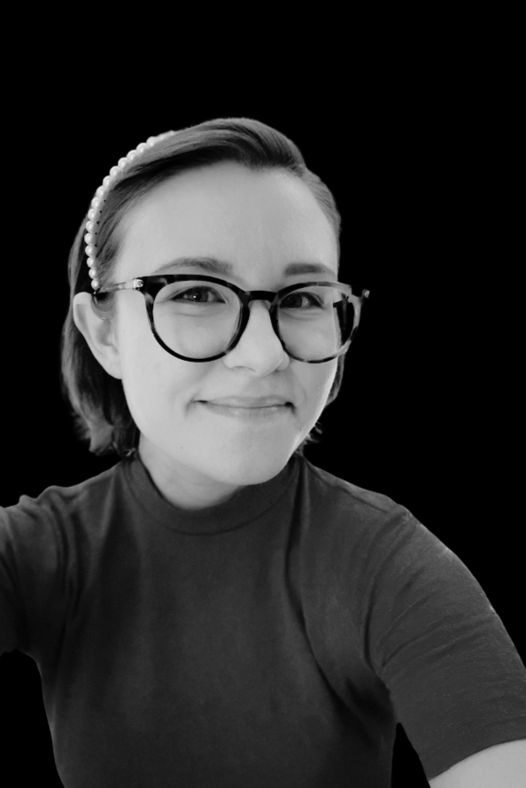 A young woman with short hair wearing glasses, a pearl headband, and a dark shirt, smiling against a black background.