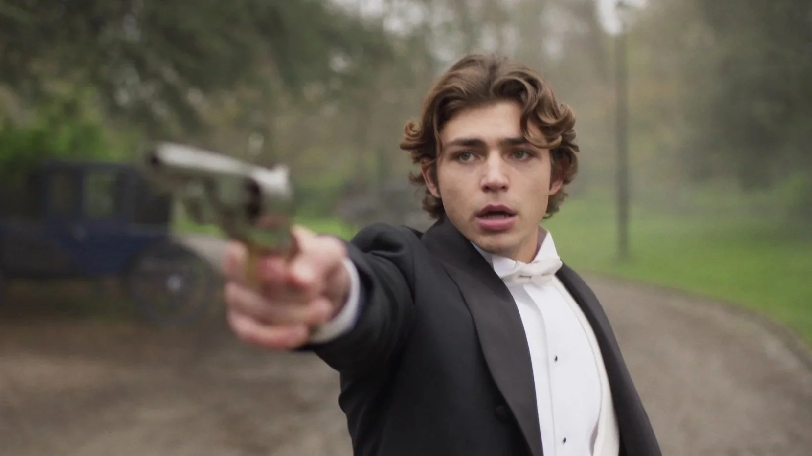 Man in tuxedo aiming a silver handgun outdoors.
