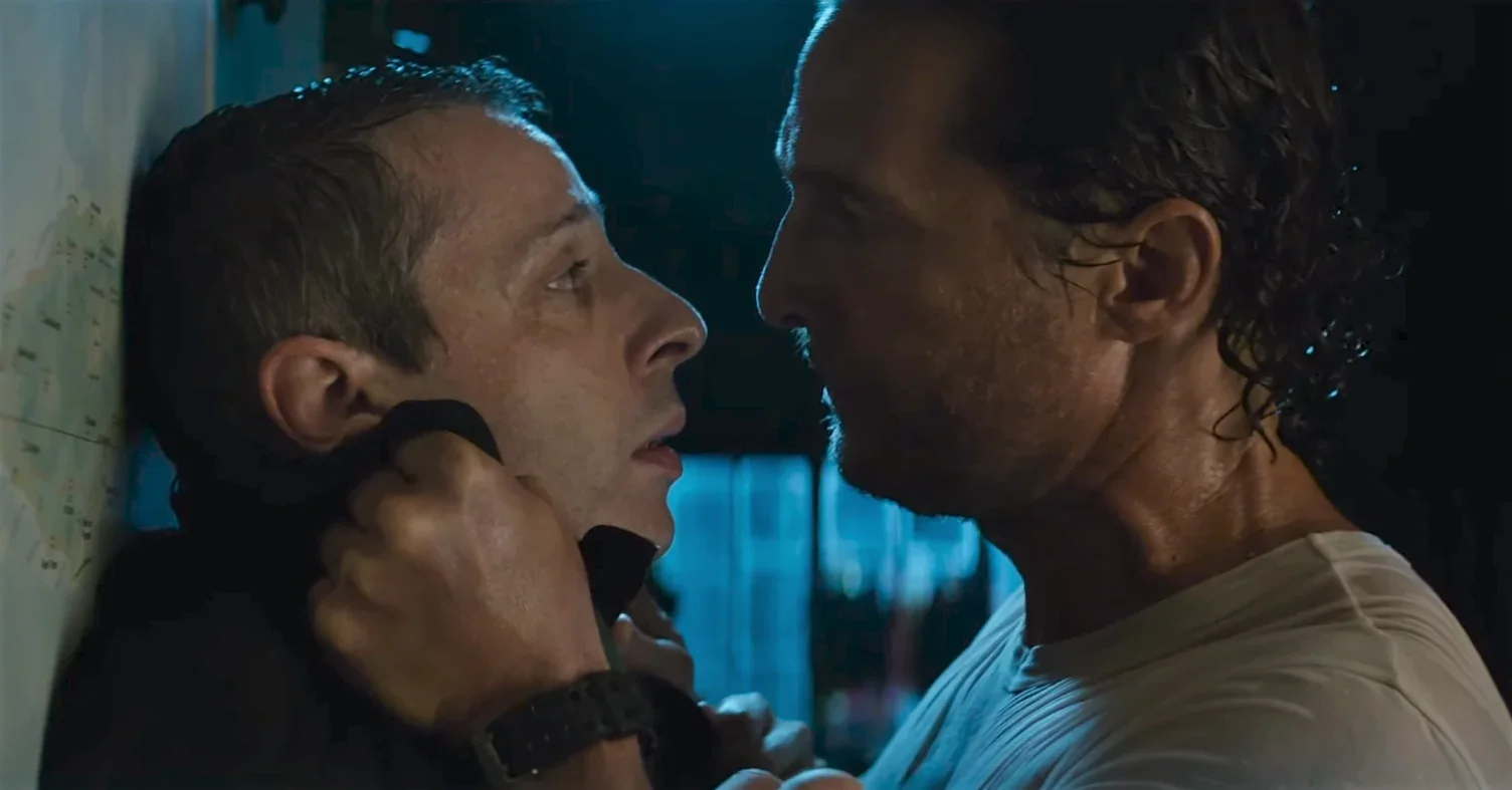 Two men are in a tense confrontation, close to each other. One man is holding the other by the collar, and they are intensely staring at each other.