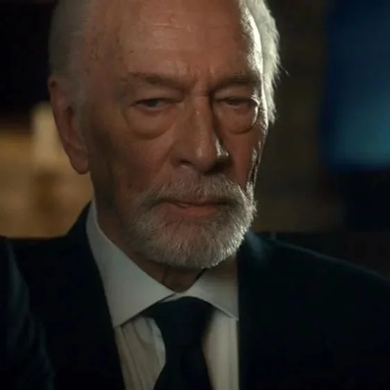 Close-up of an elderly man with white hair, beard, and mustache, wearing a suit and tie, with a serious expression.