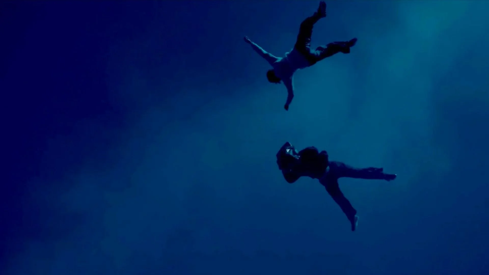 Two people floating underwater, holding hands, with a blue gradient background.
