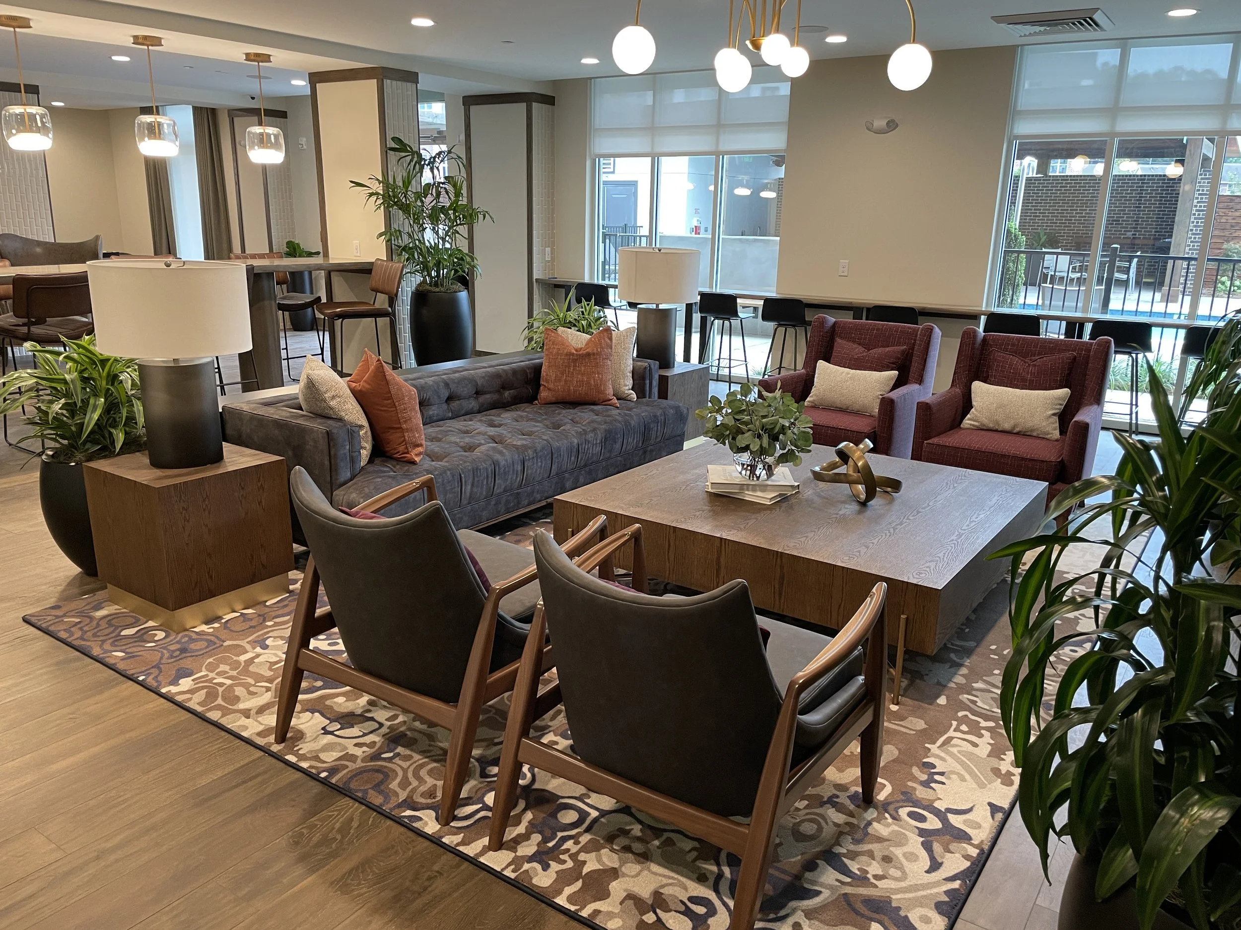 Modern lounge or waiting area with sofa, armchairs, coffee table, lamps, and decorative plants.