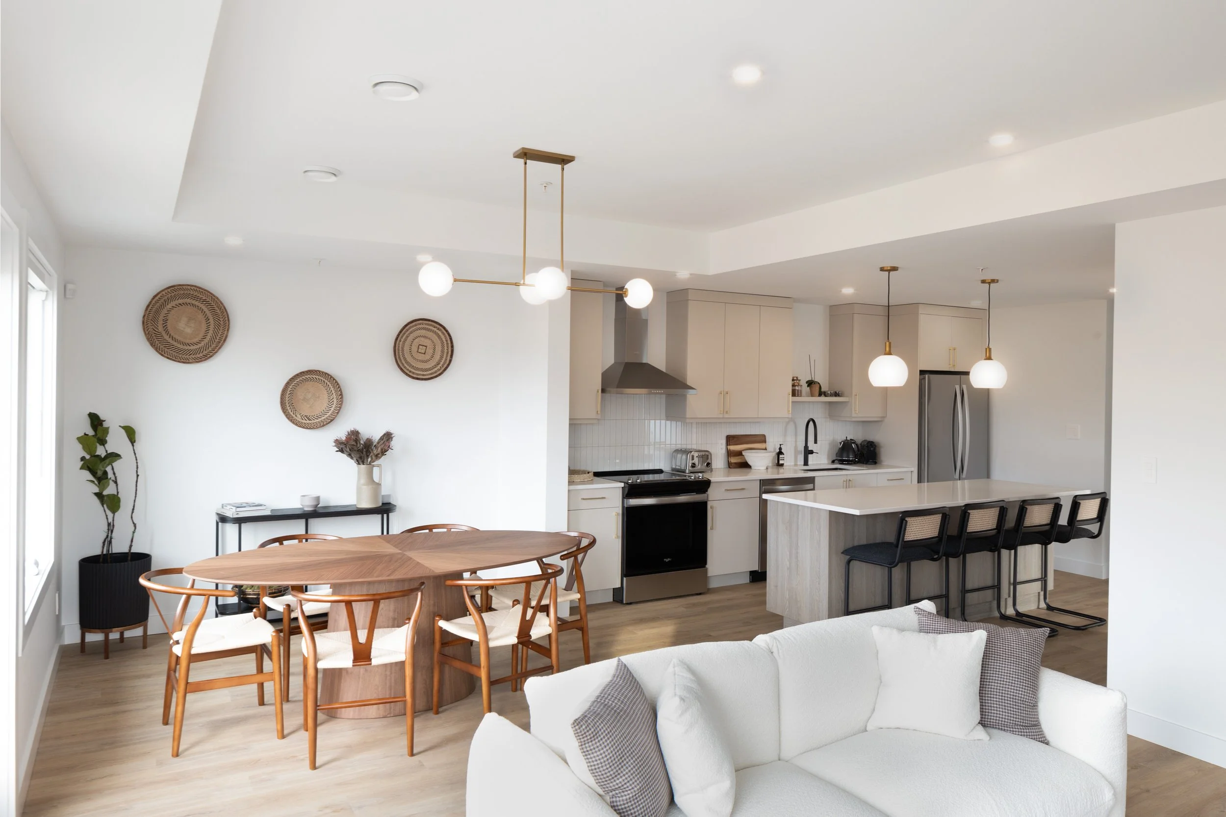 Open-concept living room and kitchen with white walls, wooden floors, modern furniture, and pendant lighting.