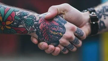 Two people shaking hands, both with colorful tattooed arms.