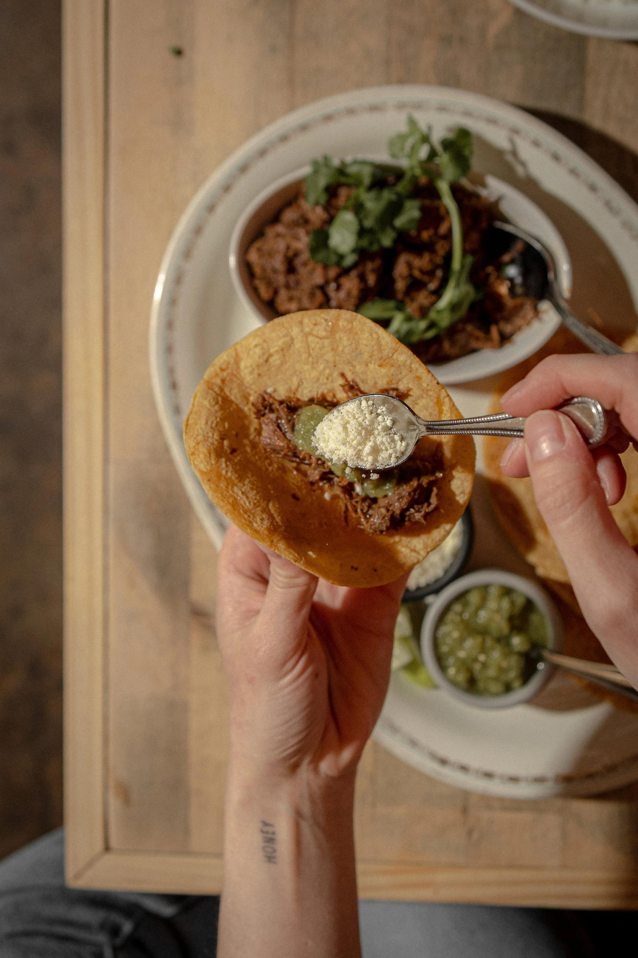 Person holding a taco with ground beef, grapes, and cheese. In the background, there is a plate with more ground beef, cilantro, and additional condiments.