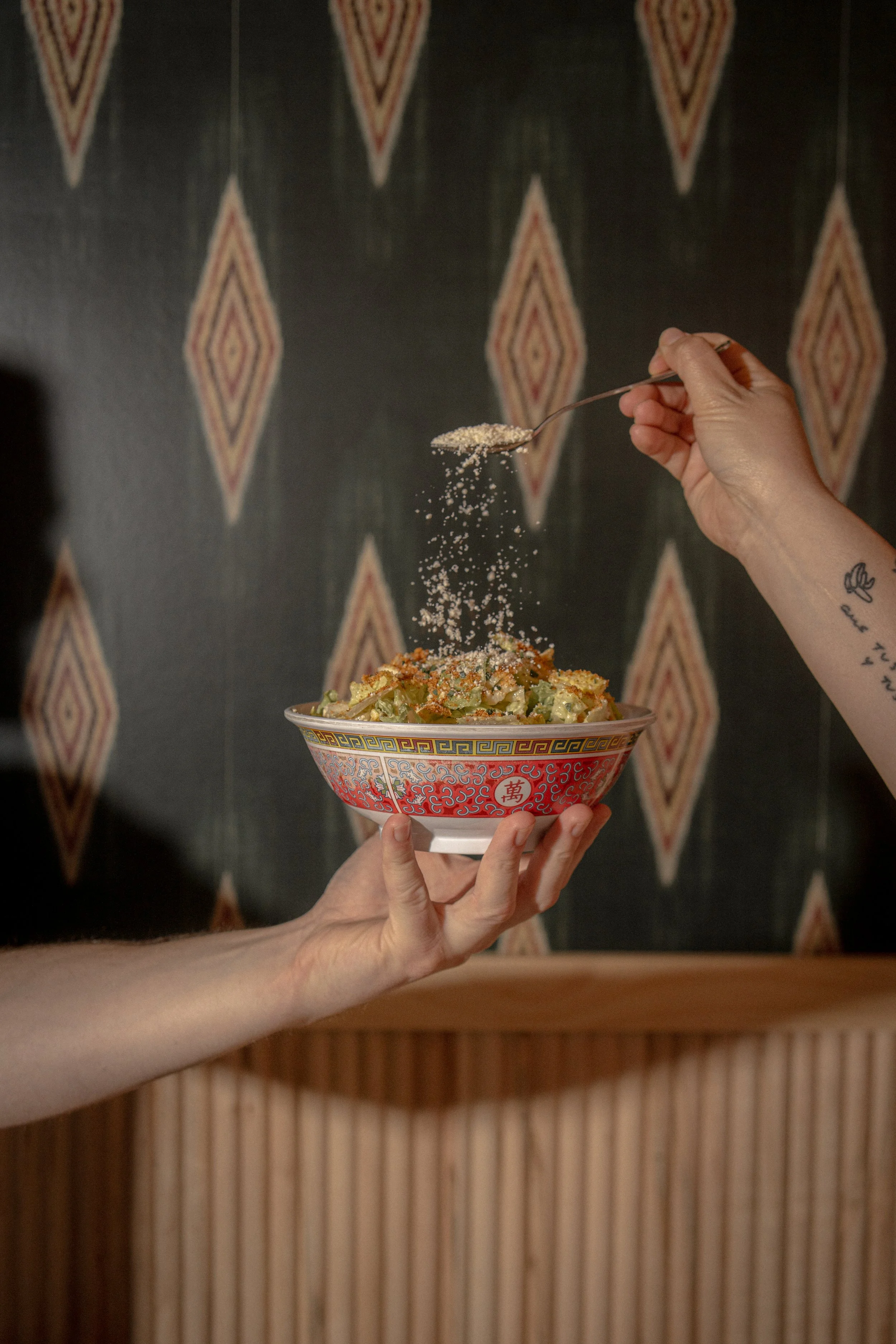 Someone is sprinkling pepper onto a bowl of Asian-style noodle salad held by another person.