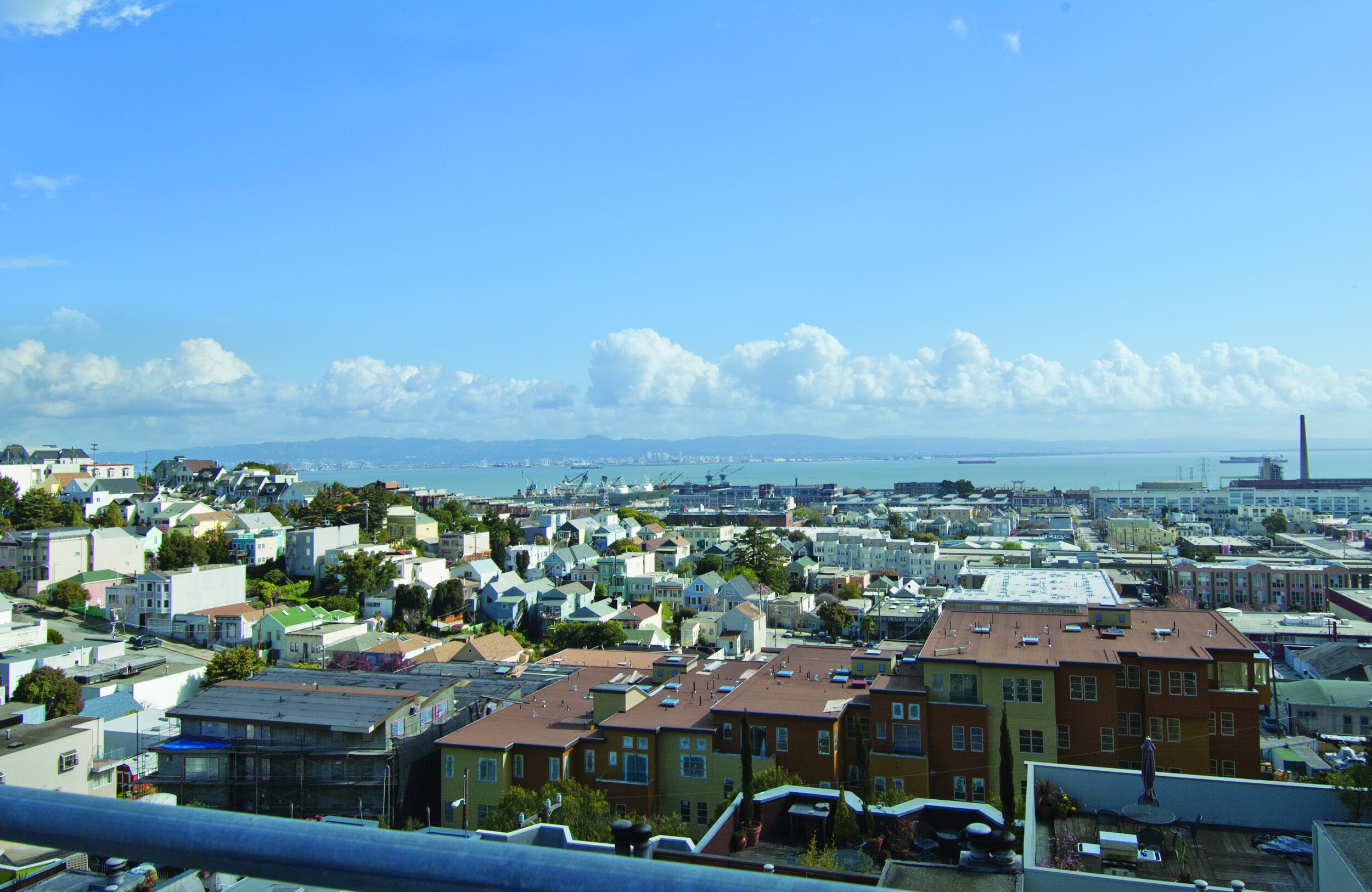 Cityscape with colorful houses, water in the distance, and a partly cloudy sky.