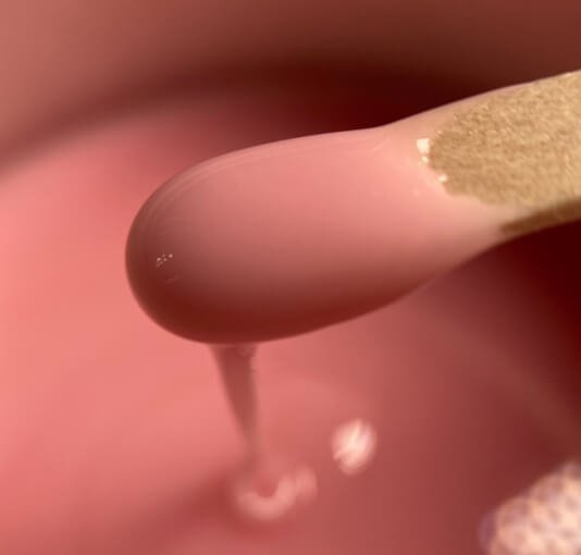 Close-up of a pink plastic swab with a liquid droplet falling from it.