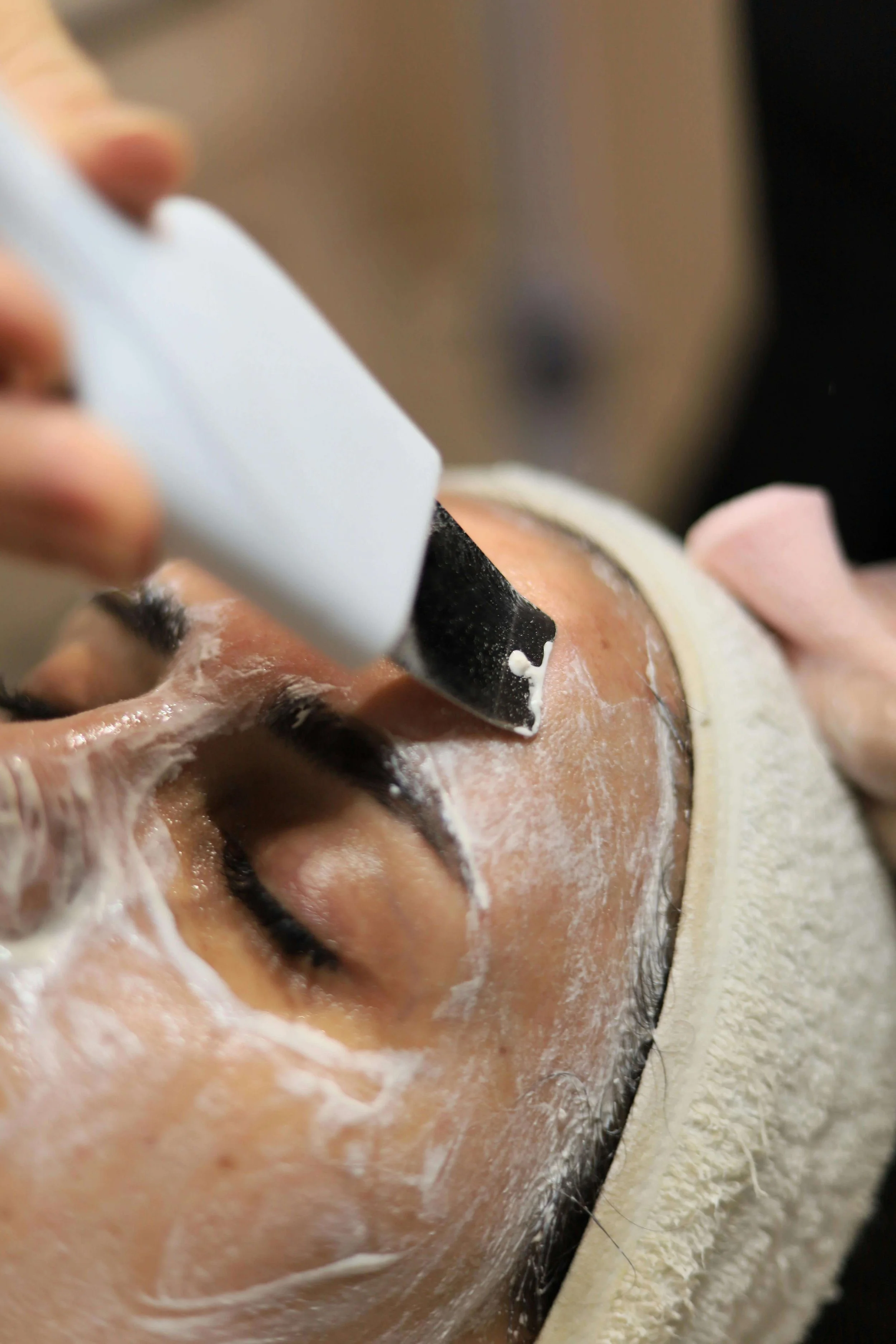A person receiving a facial treatment with a black facial tool and a white cream applied to their face.