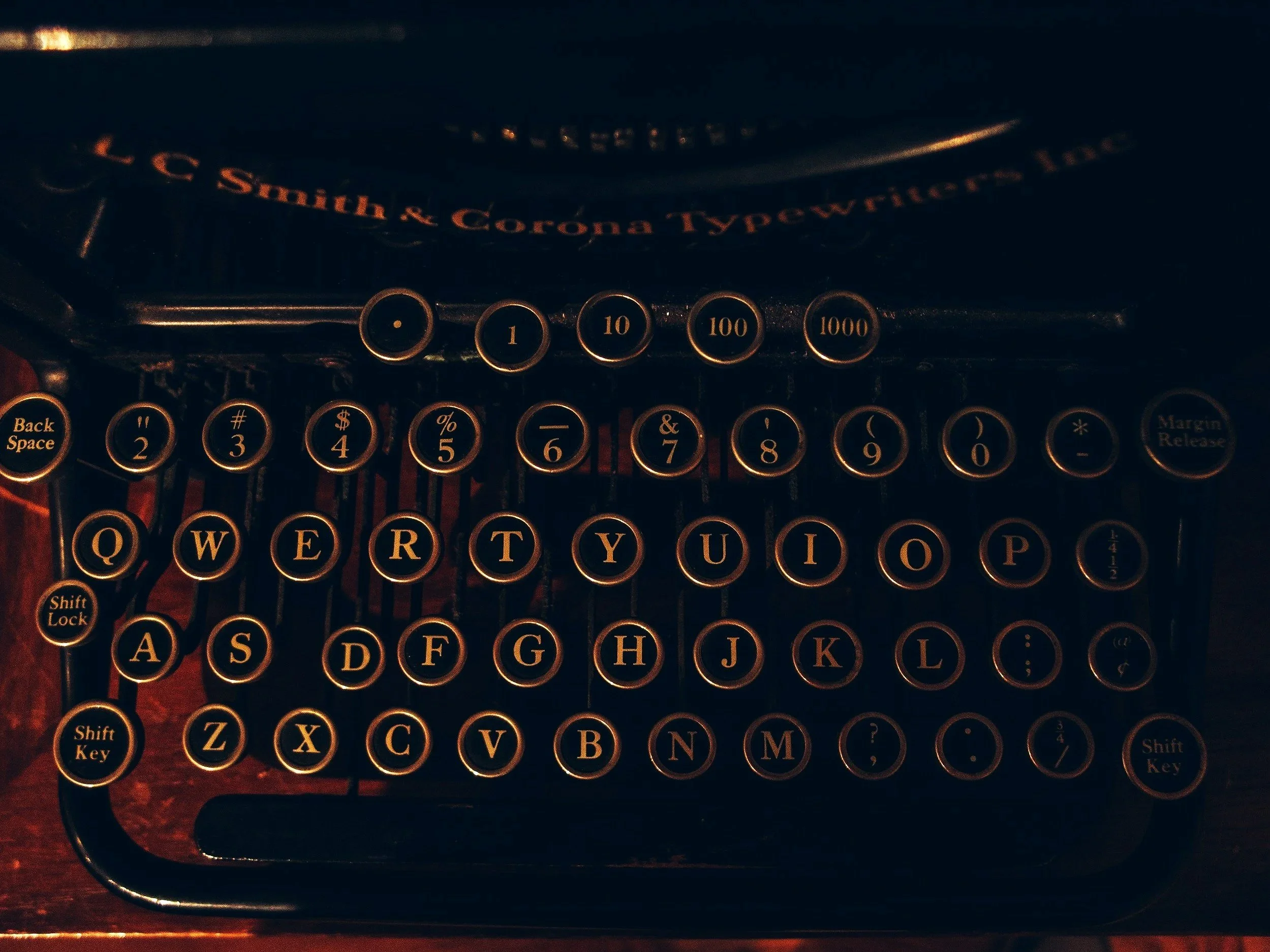 A vintage black typewriter with round keys and gold lettering, displaying the brand name "L.C. Smith & Corona Typewriters Inc."