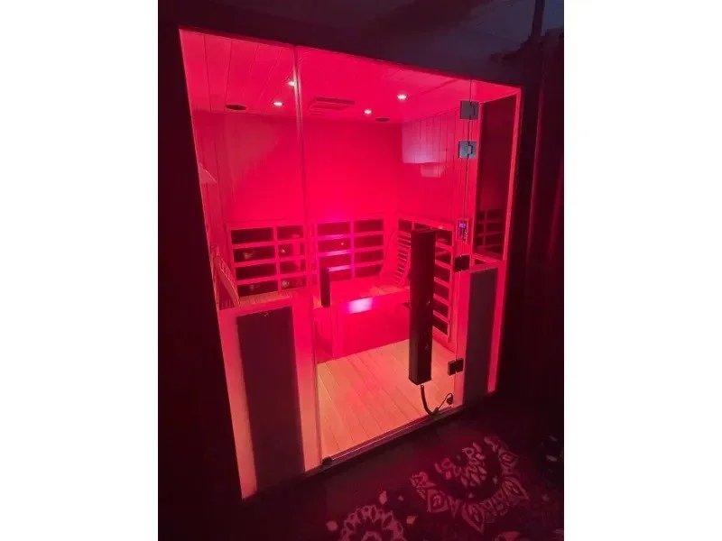 A glass sauna room illuminated with pink lighting, showing wooden benches and a towel rack inside.