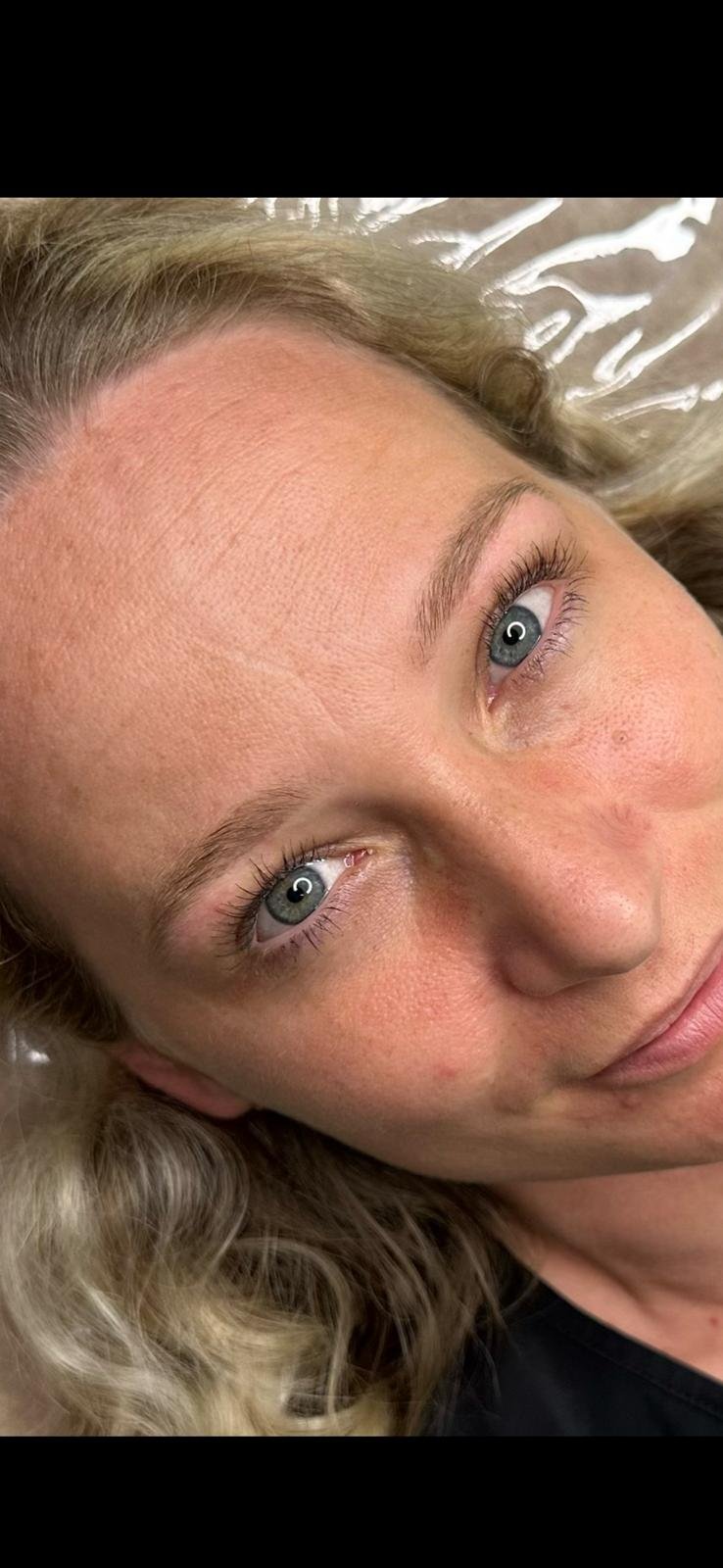 Nahaufnahme eines gesichteten Mädchens mit blauen Augen, blonden wuscheligen Haaren, heller Haut und natürlicher Hauttextur, liegend auf einem weißen Obermaterial.