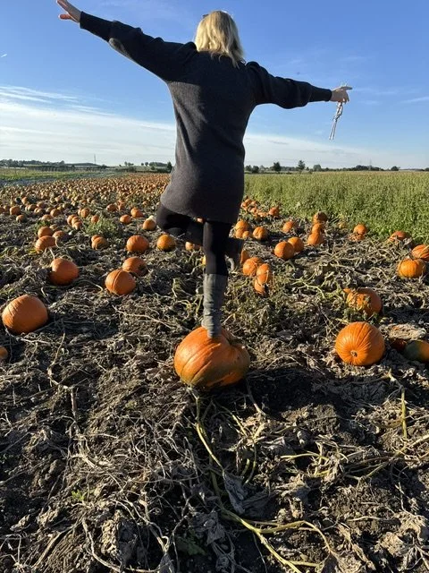 Frau tanzt auf Pumpkinfield bei Sonnenuntergang, umgeben von Kürbissen.