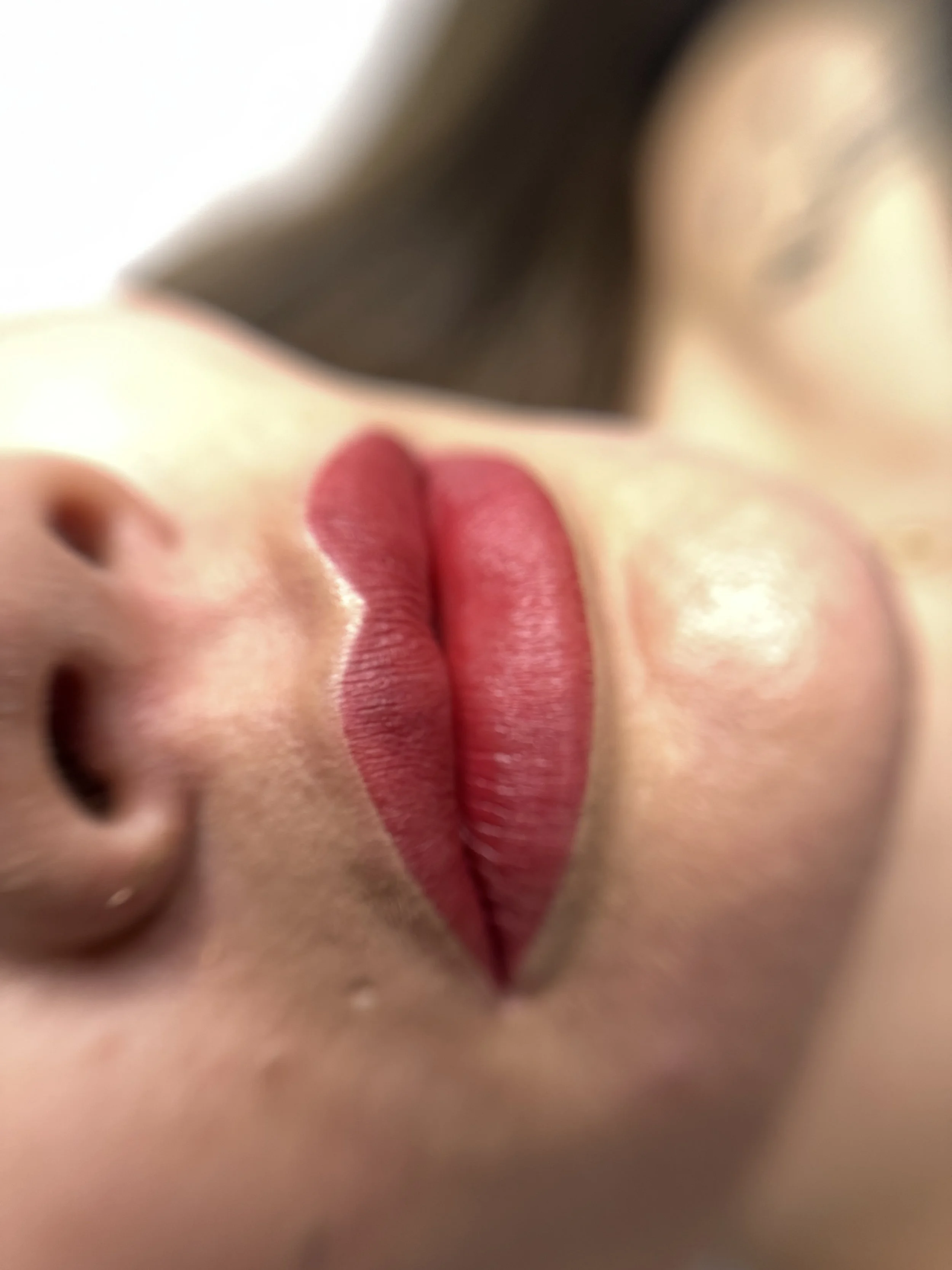 Nahaufnahme von roten Lippen, die eine Primelblüte berühren.