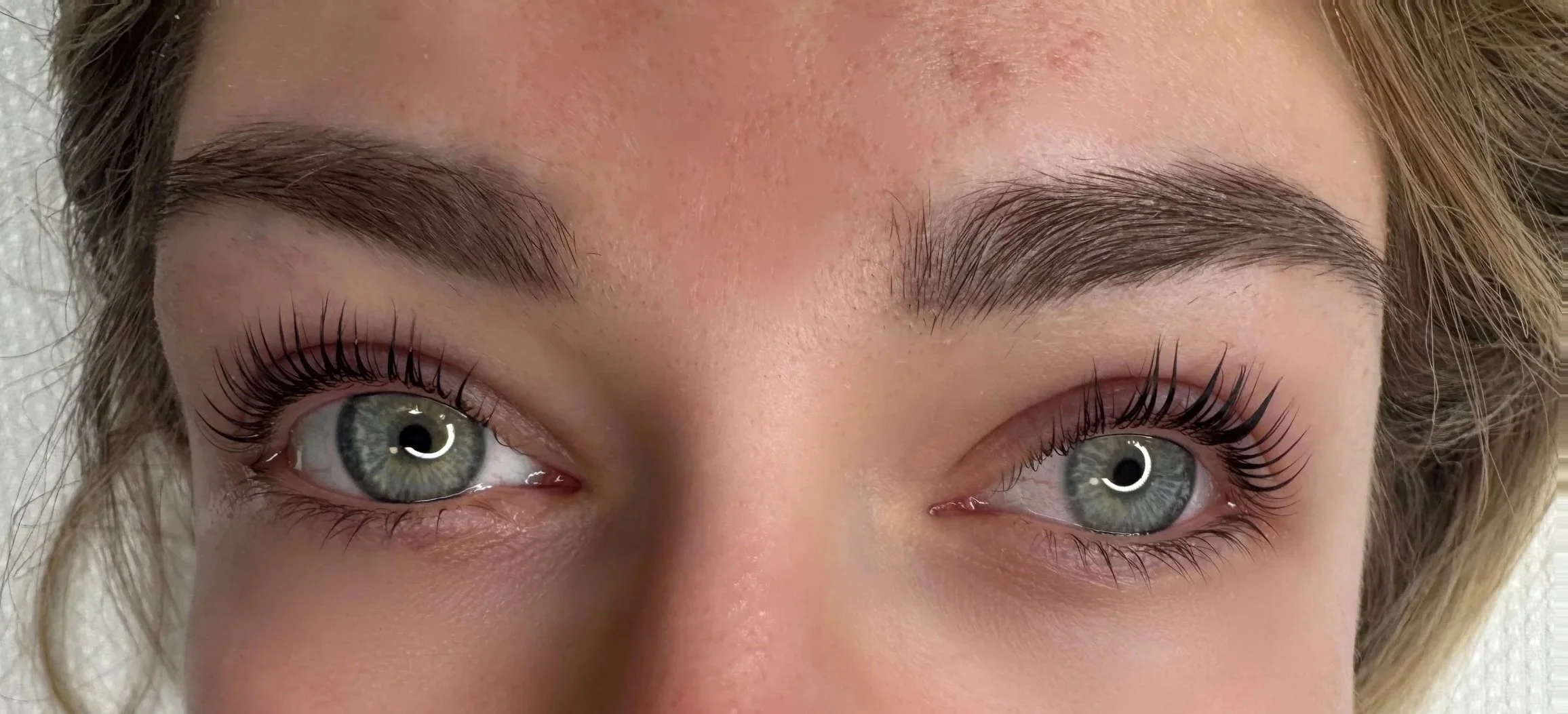 Nahaufnahme eines Gesichts mit blauen Augen, langen Wimpern und gepflegten Augenbrauen.