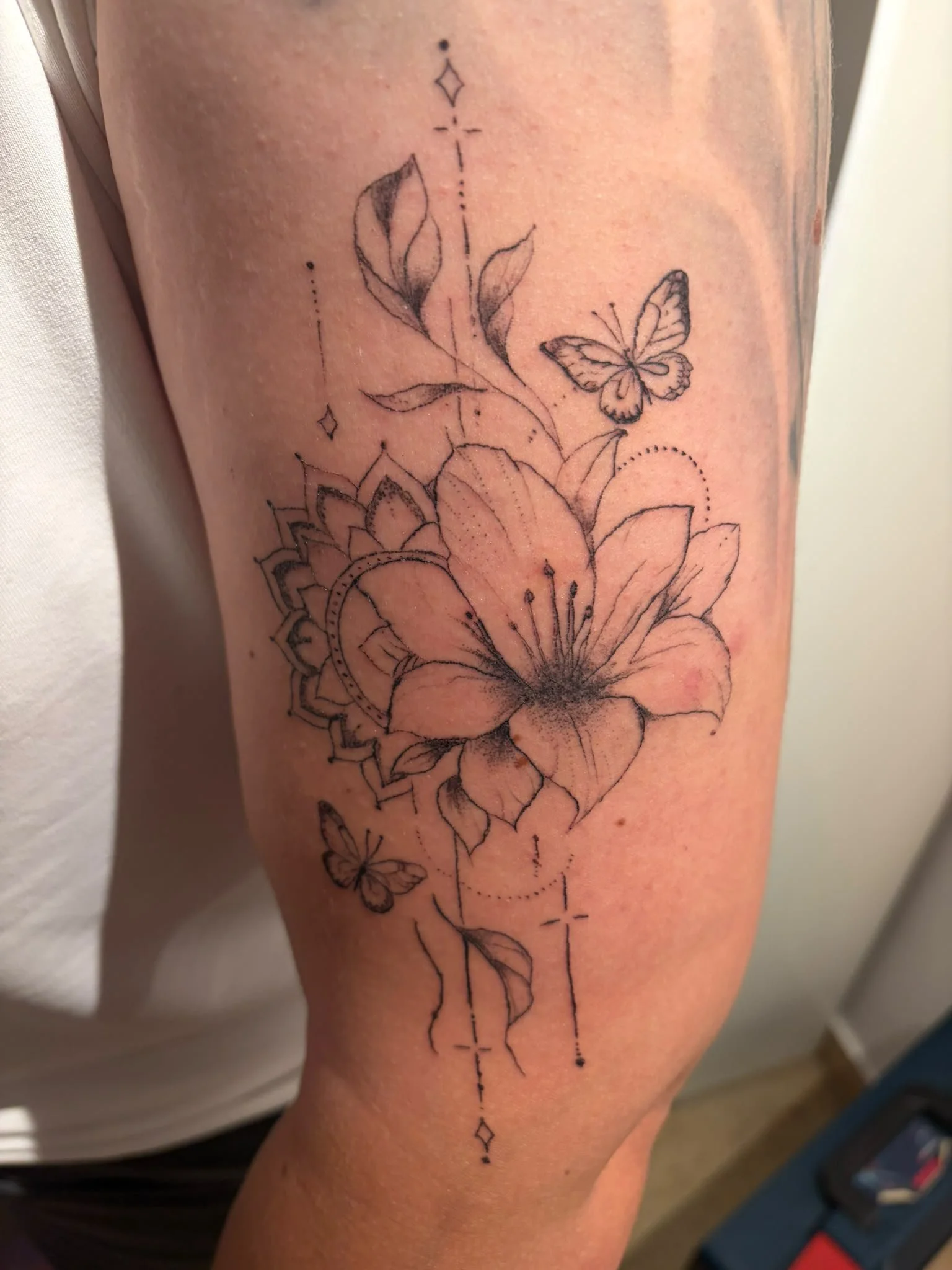Fine Line Tattoo mit Schmetterling und floralen Elementen in der Heilphase bei VOI SCHEE in Weichs