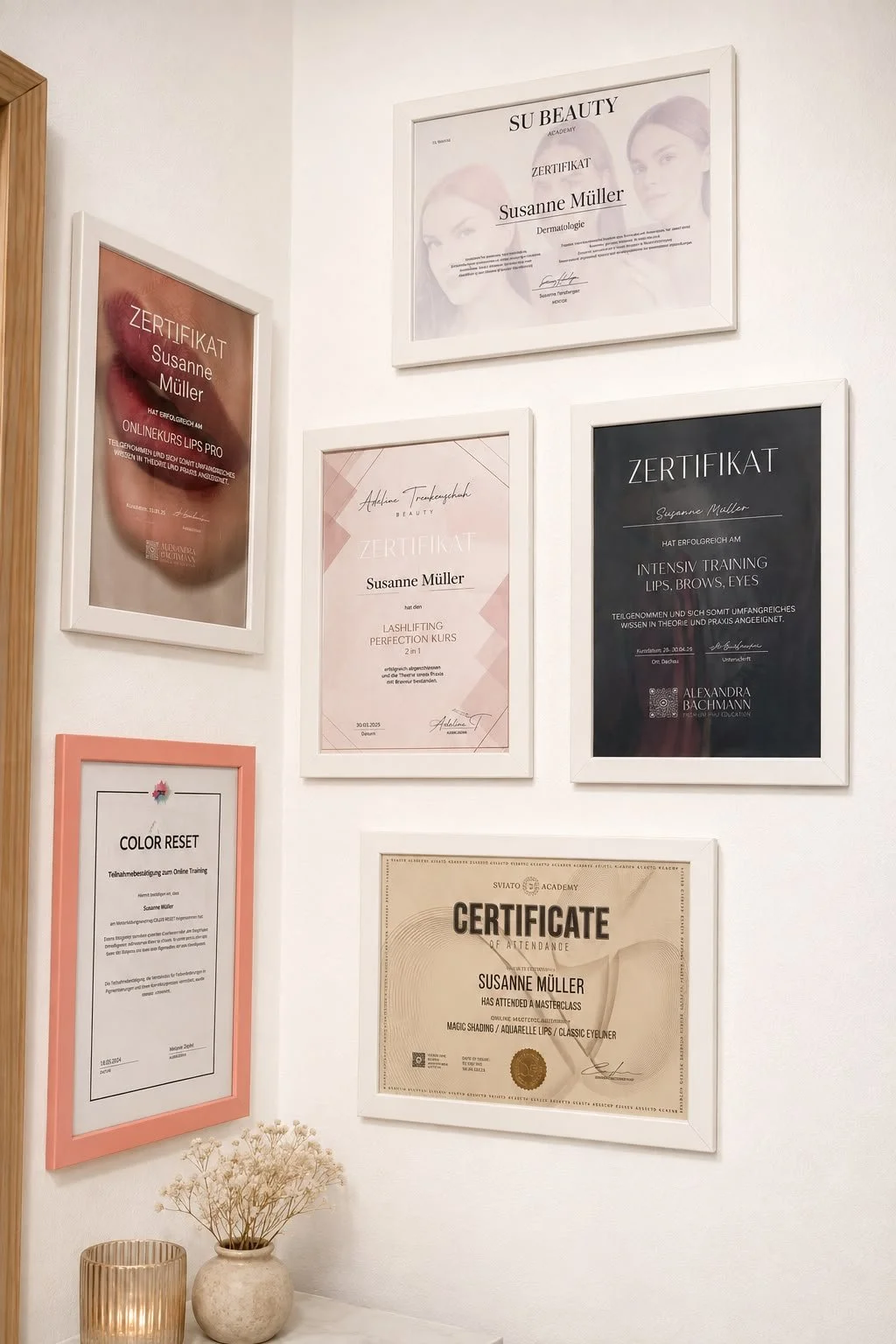 Eine Wand mit mehreren gültigen Zertifikaten für Selbsterfahrung und Beauty-Schulungen, darunter Lippen- und Augenbrauenbehandlungen, in weißen Rahmen. Im Vordergrund ein Blumentopf mit trockenen Blumen und eine Kerze.