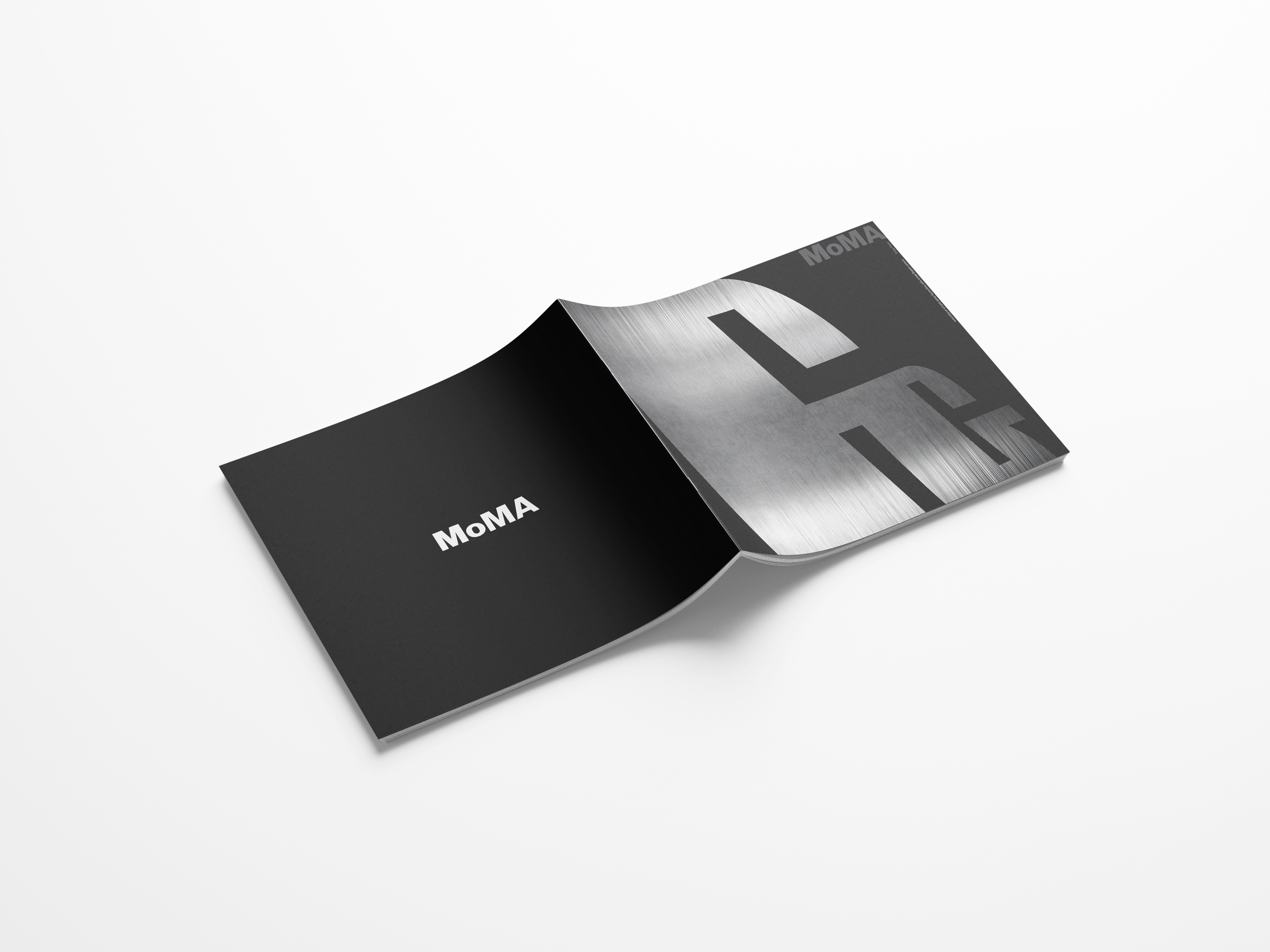 Open black booklet with 'MoMA' written on the front cover, revealing a metallic abstract design on the inside pages, placed on a white surface.
