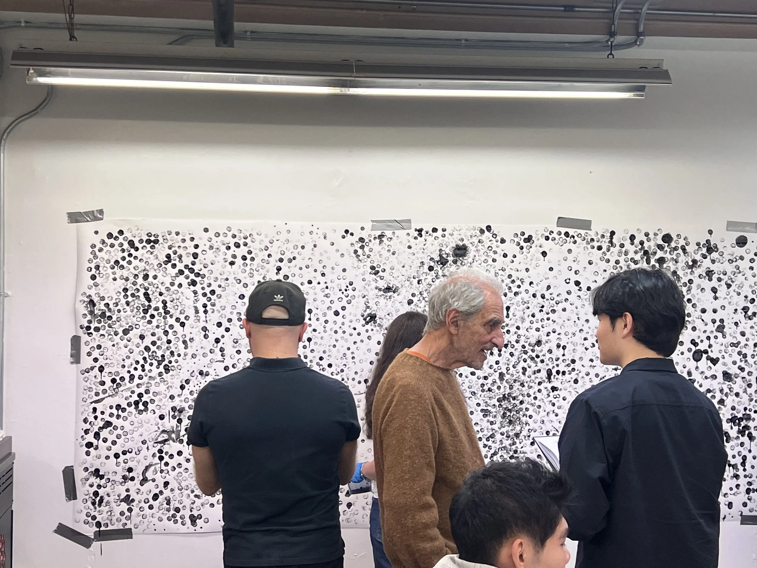 People standing in front of an abstract black-and-white artwork on a wall, engaging in conversation.