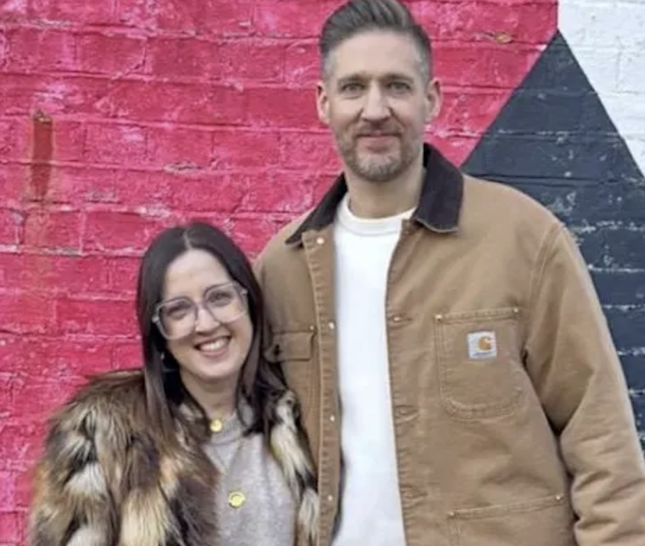 Image of a white man and woman with brown hair, smiling by a colourful wall