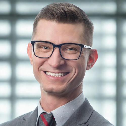 Dr. Danny Glassmann, The Leadership Alchemist, smiling and wearing glasses, a suit, and a tie.