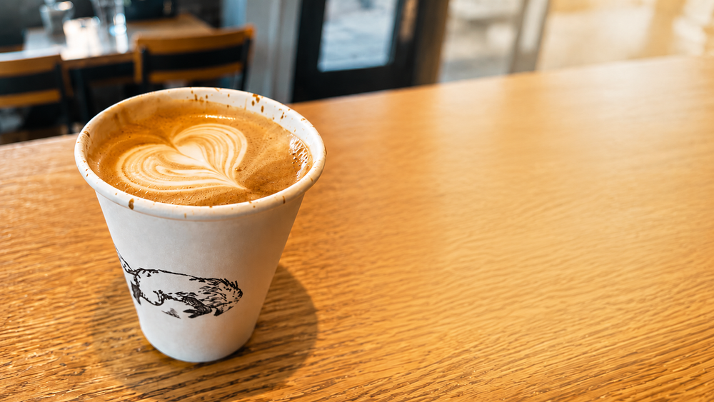 Latte with heart-shaped foam on a coffee shop table, representing the human judgment and care that should remain at the center of AI fluency.