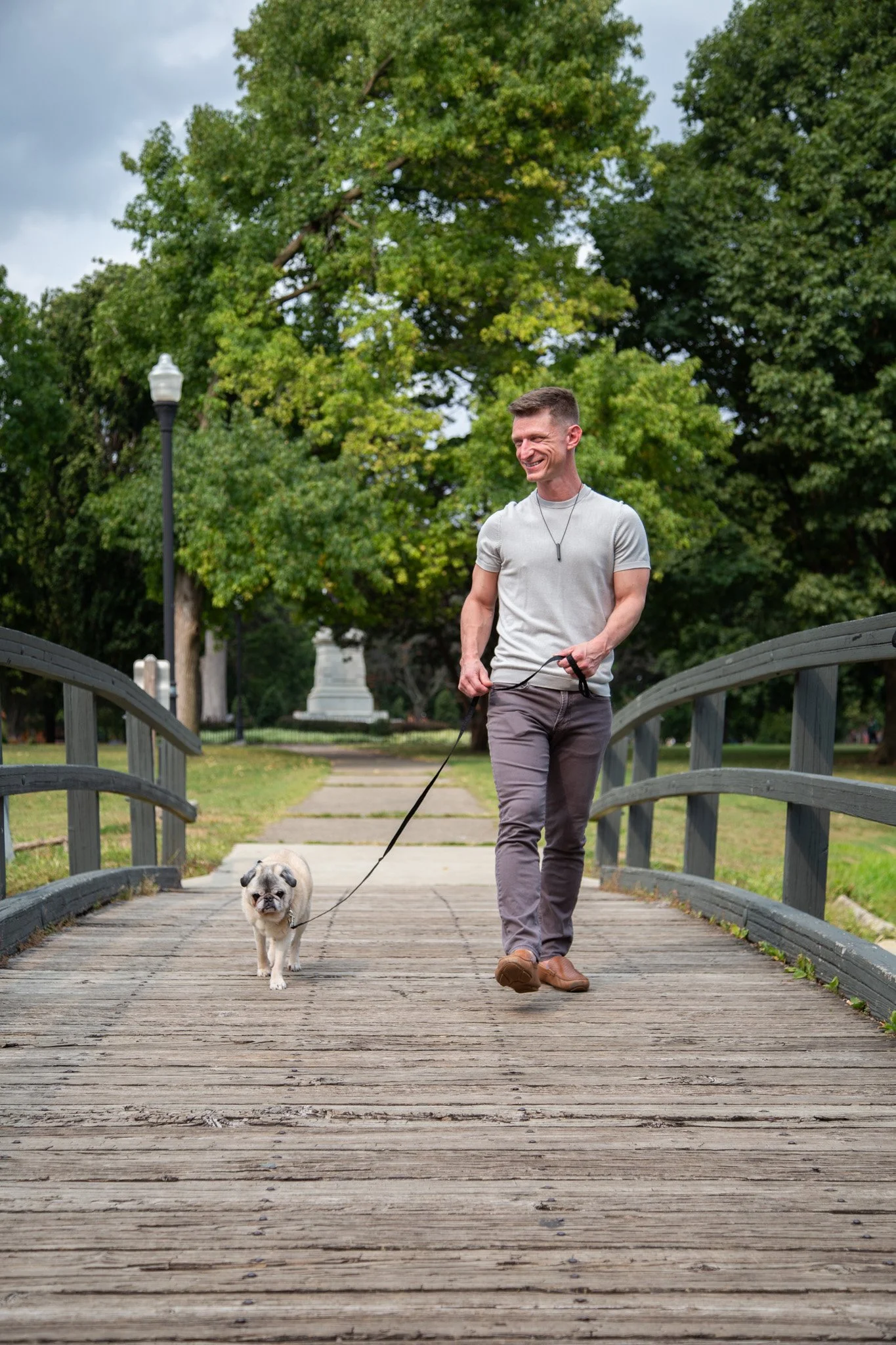 Mr. Cooper the (Peace & Belonging) Pug and Dr. Danny G. walking across a bridge in Schiller Park, Columbus, Ohio in Autumn 2025. Photo by Alec Cheravitch.